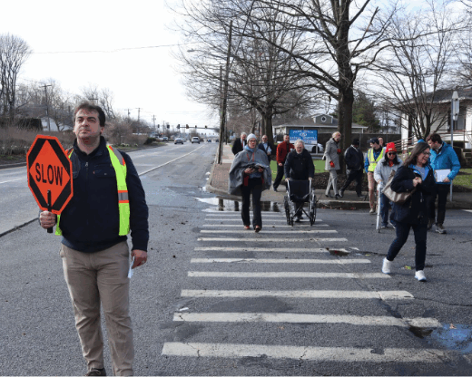 A man holds a stop sign at a crosswalk as several people cross behind him